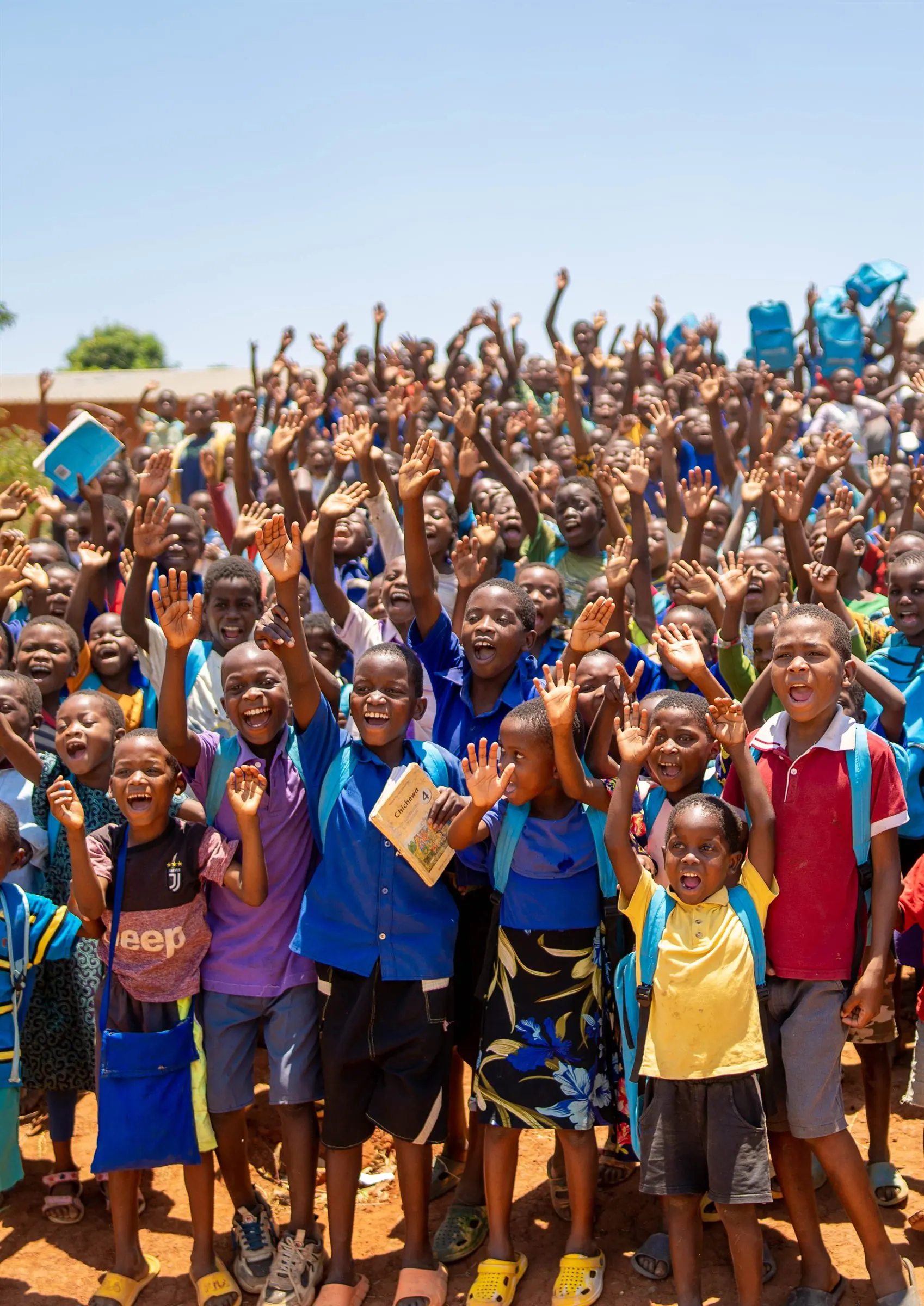 A crowd of joyful Malawian schoolchildren with their hands raised